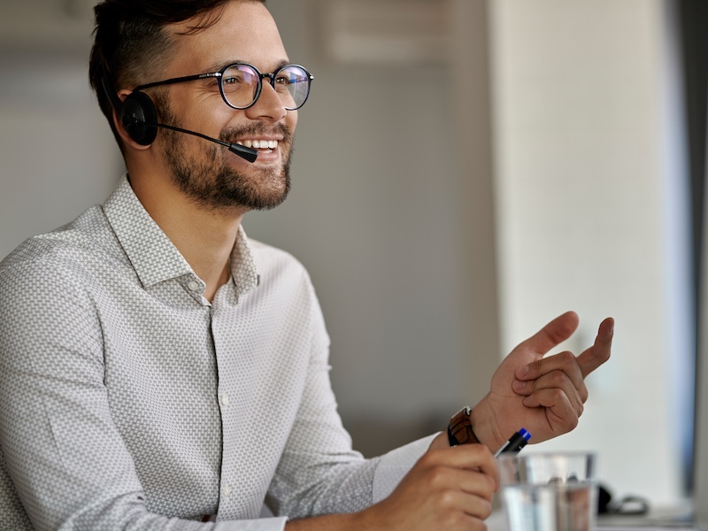 Bild eines Sympatischen Mannes am Laptop mit Headset der Lächelt 
