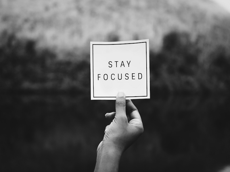 Schwarz Weiss Bild einer Hand die einen Notizzettel hält. Stay Focused steht darauf 